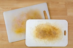 Dirty white plastic cutting board with dark stains, scratch, on wooden background