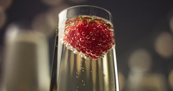 Red strawberry floating in bubbles in a glass of sparkling wine on gray background