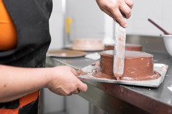 Woman pastry chef finishing chocolate cake with icing, final stage of cooking. The process of making the chocolate cake. High quality photo