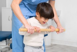 Physiotherapist and kid walking in rehabilitation center. Doctor supports a children with cerebral palsy during physiotherapy treatment. High quality photo.