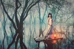 Brave woman in fairy forest foggy floats on a raft with a lantern. Alone girl looking for a way in the dark.