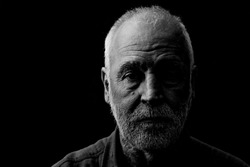 Black and white portrait of an old man, marked by life, looking thoughtfully into the camera.