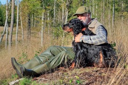 A hunter sits with his dog on a clearing and enjoys the warm sun rays
