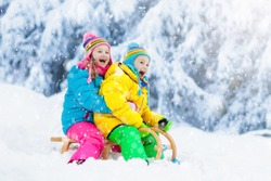 Little girl and boy enjoying sleigh ride. Child sledding. Toddler kid riding a sledge. Children play outdoors in snow. Kids sled in snowy park in winter. Outdoor fun for family Christmas vacation.