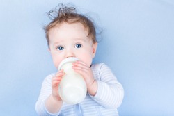 Sweet little baby with beautiful blue eyes drinking milk in a plastic bottle relaxing on a blue knitted blanket