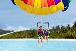 Kids parasailing. Water sport on summer vacation. Brother and sister flying in tropical ocean resort. Sea and beach fun. Rainbow parachute. Teenage boy and little girl fly.
