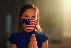 Pray for America. Child in face mask praying for USA. Little American girl in hospital chapel or church during coronavirus outbreak. Virus pandemic. Children say a prayer for sick patient.