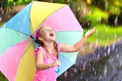 Kid playing out in the rain. Children with umbrella play outdoors in heavy rain. Little girl caught in first spring shower. Kids outdoor fun by rainy autumn weather. Child running in tropical storm.