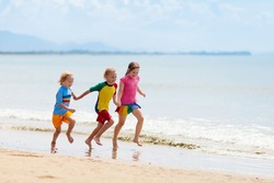Kids playing on tropical beach. Children swim and play at sea on summer family vacation. Sand and water fun, sun protection for young child. Little boy running and jumping at ocean shore.