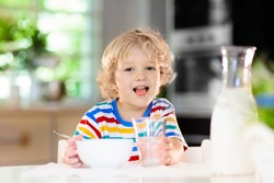Child having breakfast. Kid drinking milk and eating cereal with fruit. Little boy at white dining table in kitchen at window. Kids eat on sunny morning. Healthy balanced nutrition for young kids.