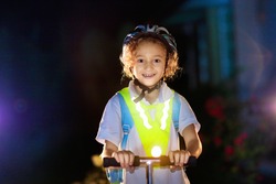 Kid in reflective vest in darkness. Safety on dark city streets for school children. Safe way home at night or in the evening. Fluorescent stripes on kids clothing and backpack. Boy walking at dusk.