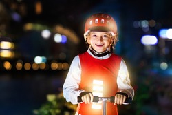 Kid in reflective vest in darkness. Safety on dark city streets for school children. Safe way home at night or in the evening. Fluorescent stripes on kids clothing and backpack. Boy walking at dusk.