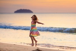Child playing on ocean beach. Kid jumping in the waves at sunset. Sea vacation for family with kids. Little girl in beautiful dress running on tropical beach of exotic island during summer holiday.