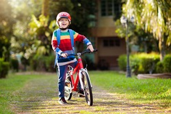 Child going to school on bike. Kids ride bicycle. Safe way to elementary school. Little boy with backpack on red bike wearing safety helmet. Healthy outdoor activity for young student.