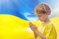 Pray for Ukraine. Child with Ukrainian flag. Little blond boy waving national flag praying for peace. Happy kid celebrating Independence Day.