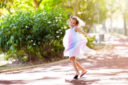 Happy kid playing in summer park. Little girl dancing in beautiful dress. Children run, spin, twirl and laugh. Summer vacation fun. School holiday activity. Easter or child birthday party.