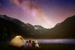 Family camping under starry night sky. Milky way watching. Camp bonfire with kids. Travel and hiking with young children and dog. Group of people next to tent in national park. Star gazing.