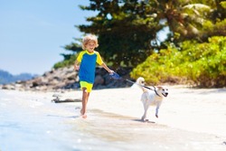 Child and dog playing on tropical beach. Little boy running with his puppy. Family summer vacation on sea side. Travel with children and pet. Holiday with kids and animal. Active healthy kid.