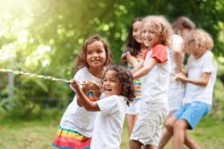 Kids play tug of war in sunny park. Summer outdoor fun activity. Group of mixed race children pull rope in school sports day. Healthy outdoor game for little boy and girl.