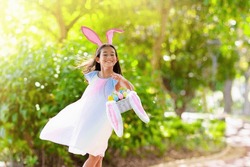 Easter egg hunt. Little girl with bunny ears celebrating Easter. Kids celebrate spring holiday. Children search chocolate eggs and candy. Rabbit costume. Christian holidays with child.