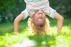 Little boy hanging upside down. Handstand exercise for little kids. Active child playing on sunny garden lawn. Summer fun. Kids play outdoor. Healthy sports activity in beautiful park.