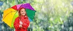 Kid playing in the rain in autumn park. Child with umbrella and rain boots play outdoors in heavy rain. Little girl in red jacket under fall shower. Kids fun by rainy weather. Children play in storm.