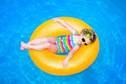 Cute funny little toddler girl in a colorful swimming suit and sun glasses relaxing on an inflatable toy ring floating in a pool having fun during summer vacation in a tropical resort 