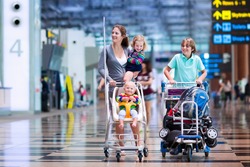 Family traveling with kids. Parents with children at international airport with luggage in a cart. Mother holding baby, toddler girl and boy flying by airplane. Travel with child for summer vacation.