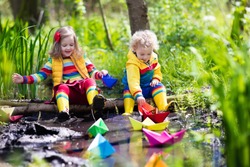 Children play with colorful paper boats in a small river on a sunny spring day. Kids playing exploring the nature. Brother and sister having fun at a forest stream. Boy and girl with toy boat and ship