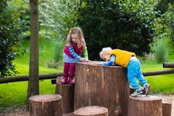 Little boy and girl climbing on a wooden playground in a park. Kids play outdoors on cold autumn day.
