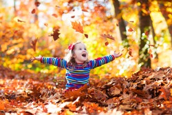 Happy little girl playing in beautiful autumn park on warm sunny fall day. Kids play with golden maple leaves.