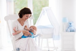 Mother and baby at home. Breastfeeding and healthy infant nutrition. Young woman nursing her newborn child in rocking chair in sunny nursery with crib and garden view window. Parent and kid at home