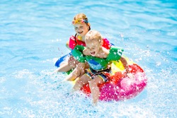 Boy and girl on inflatable ice cream float in outdoor swimming pool of tropical resort. Summer vacation with kids. Swim aids and wear for children. Water toys. Little child floating on colorful raft.