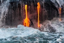 Molten lava flowing into the Pacific Ocean on Big Island of Hawaii at sunrise, with water and lava flowing down lava rock wall as waves crash as seen from a tour boat