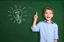 Schoolboy standing near blackboard with light bulb