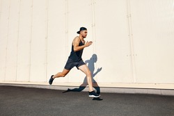 Young man runner running along wall with copy space. Sport concept