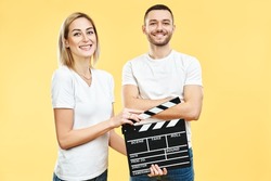 Young happy couple with cinema clapper board over yellow background. Fun, cinematography concept