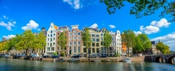 Panoramic view of Amsterdam street over the water. Famous narrow houses against the blue sky. Amsterdam, Holland, Netherlands, Europe.