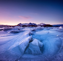 Mountain ridge and reflection on the frozen lake surface. Natural landscape on the Lofoten islands, Norway. Water and mountains during sunset.