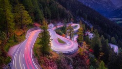 Maloja pass, Switzerland. A road with many curves among the forest. A blur of car lights. Landscape in evening time. 