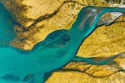 A drone view of the river on the field. An aerial view of an autumn landscape. Winding river among the meadows. Turquoise mountain water. Landscape with soft light before sunset. 