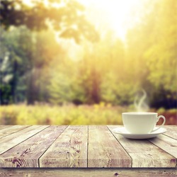 Cup with hot drink on wood table over forest  background