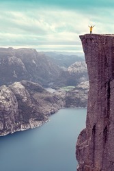 girl raised her hands up standing on the famous Preikestolen Pulpit Rock over the Lysefjord