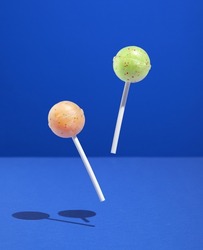 Two bright lollipops on sticks hover over blue surface. Sweet inspiration and happy mood.