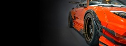 Front headlights of orange modify car on black background, copy space	
