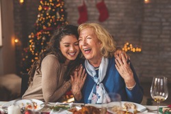 Family having Christmas dinner at home, gathered around the table, enjoying their time together; daughter hugging her mother and smiling