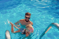 High angle view of beautiful little girl and her father having fun in the swimming pool on a hot sunny summer day, father teaching daughter to swim