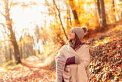 Beautiful young woman enjoying sunny autumn day in nature, walking down the forest path covered with colorful fallen leaves and relaxing, taking a breath of fresh air