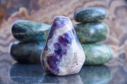 Close-up of polished pebble of white quartz and amethyst against of pebble of jade and serpentinite. Polished amethyst stone with a purple color.