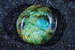 Close-up of natural gemstone polished green-blue labradorite mineral on polished dark stony slab.